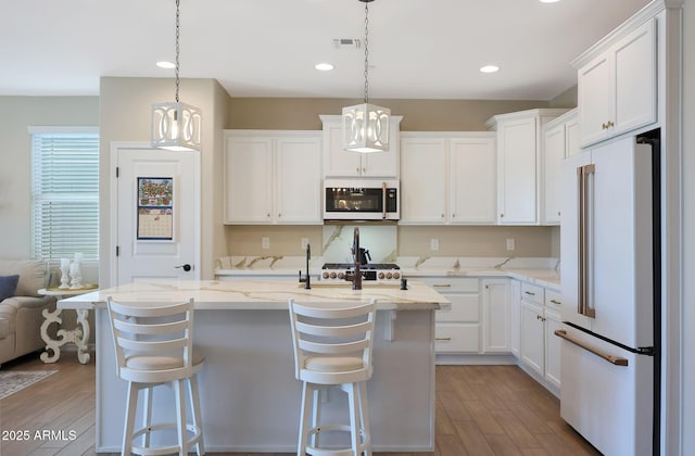 kitchen featuring pendant lighting, white appliances, a kitchen breakfast bar, white cabinets, and a center island with sink