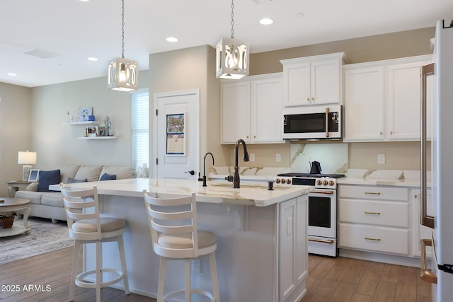 kitchen featuring pendant lighting, white appliances, white cabinets, and a center island with sink