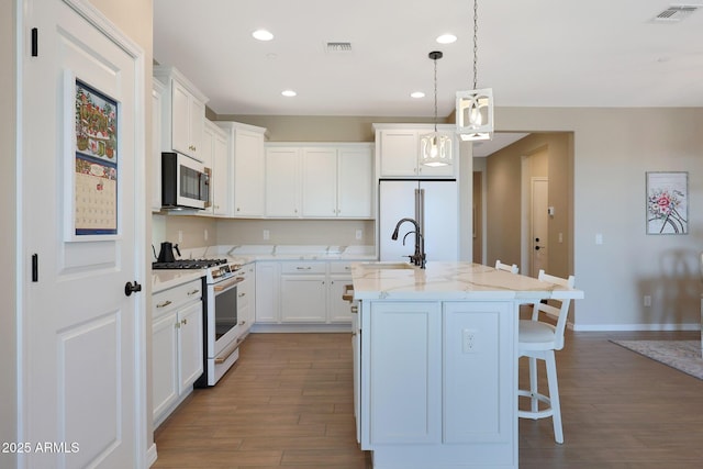 kitchen with white cabinetry, light stone counters, fridge, white range with gas cooktop, and an island with sink