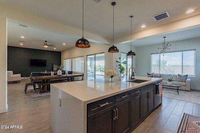 kitchen with a center island with sink, hanging light fixtures, sink, and light hardwood / wood-style flooring