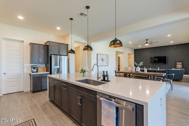 kitchen with light hardwood / wood-style floors, a kitchen island with sink, pendant lighting, sink, and appliances with stainless steel finishes