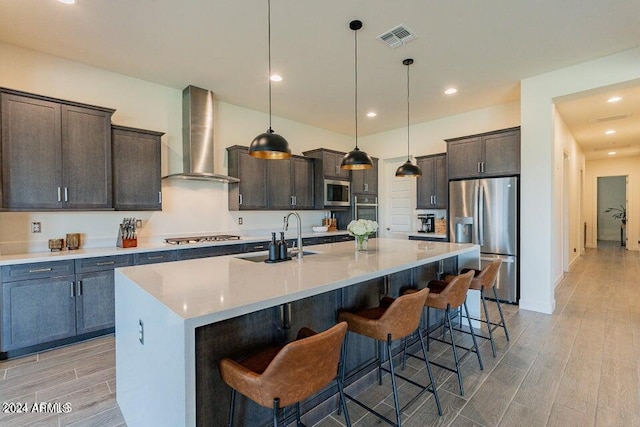 kitchen with wall chimney exhaust hood, an island with sink, appliances with stainless steel finishes, and sink