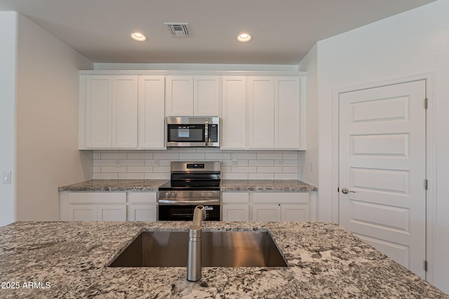 24184 W Gibson Ln, Buckeye, AZ 85326 - kitchen with stainless steel appliances, dark stone counters, white cabinets, decorative backsplash, and recessed lighting