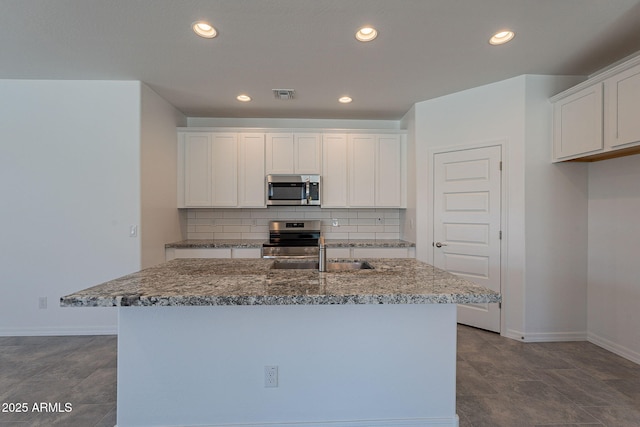 24184 W Gibson Ln, Buckeye, AZ 85326 - kitchen with appliances with stainless steel finishes, tasteful backsplash, white cabinets, recessed lighting, and a center island with sink