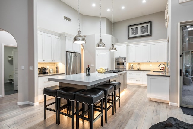 kitchen featuring visible vents, a center island, arched walkways, appliances with stainless steel finishes, and a towering ceiling