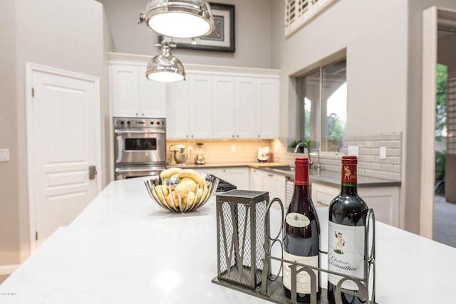 kitchen with a sink, decorative backsplash, white cabinetry, and stainless steel double oven