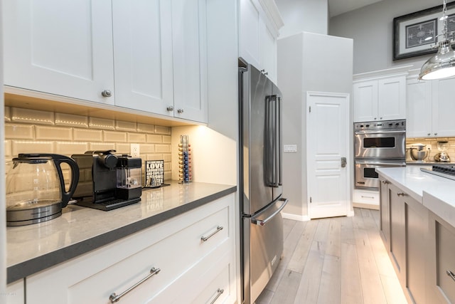 kitchen featuring tasteful backsplash, dark stone counters, light wood-style flooring, stainless steel appliances, and white cabinetry