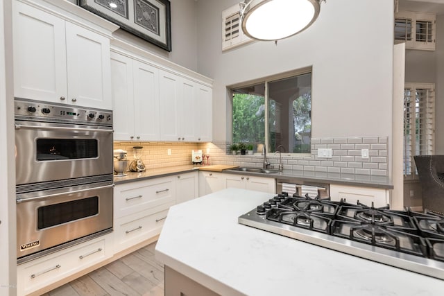 kitchen featuring stainless steel double oven, cooktop, backsplash, and a sink