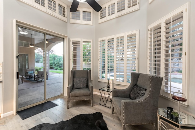 sitting room featuring baseboards, ceiling fan, wood finished floors, a high ceiling, and a sunroom