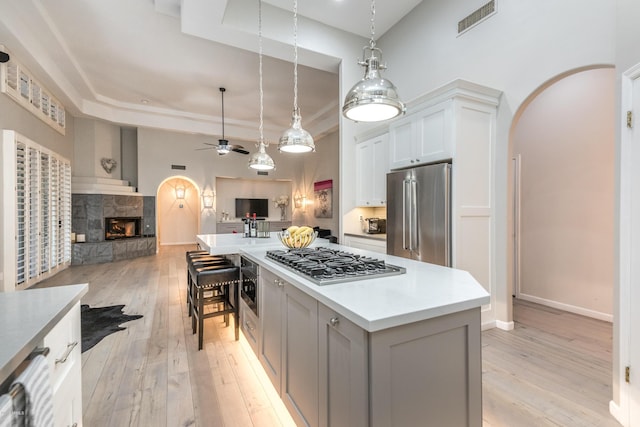 kitchen with visible vents, open floor plan, a lit fireplace, appliances with stainless steel finishes, and arched walkways