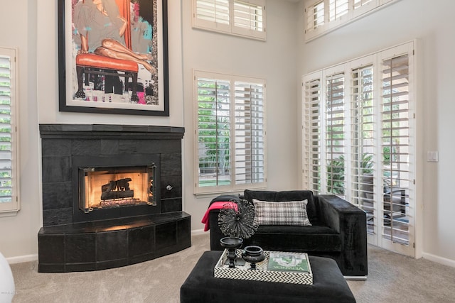 carpeted living room featuring baseboards, a towering ceiling, and a tile fireplace