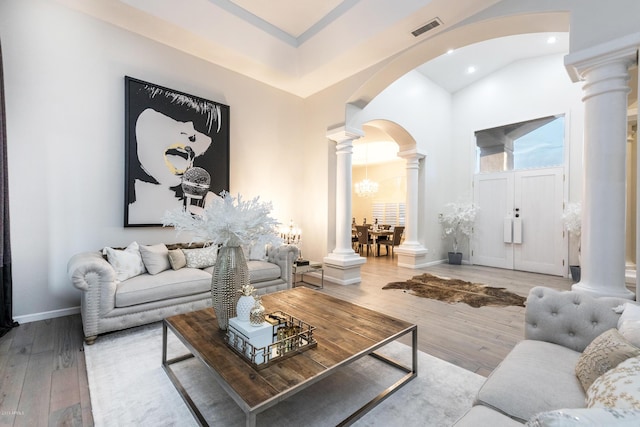 living area featuring arched walkways, visible vents, ornate columns, and wood-type flooring