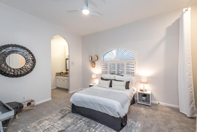 bedroom featuring ceiling fan, baseboards, light carpet, arched walkways, and ensuite bath