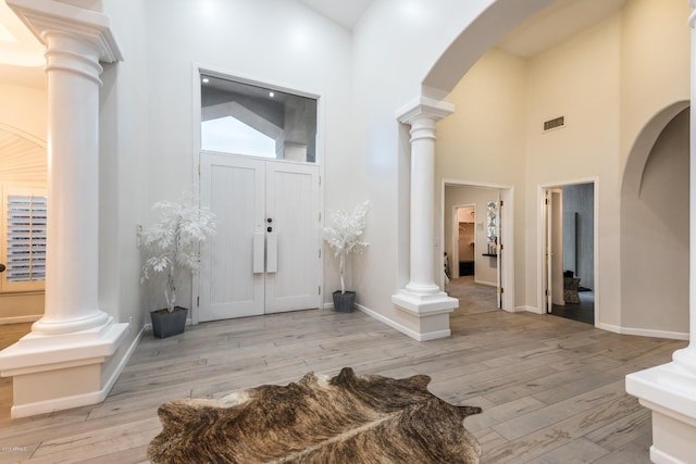 entrance foyer featuring visible vents, decorative columns, a high ceiling, arched walkways, and wood-type flooring