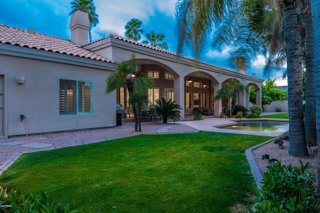 back of property with stucco siding, a lawn, an outdoor pool, a chimney, and a patio area