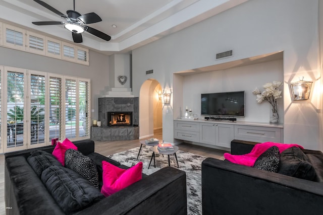 living area featuring visible vents, a tile fireplace, wood finished floors, arched walkways, and a ceiling fan