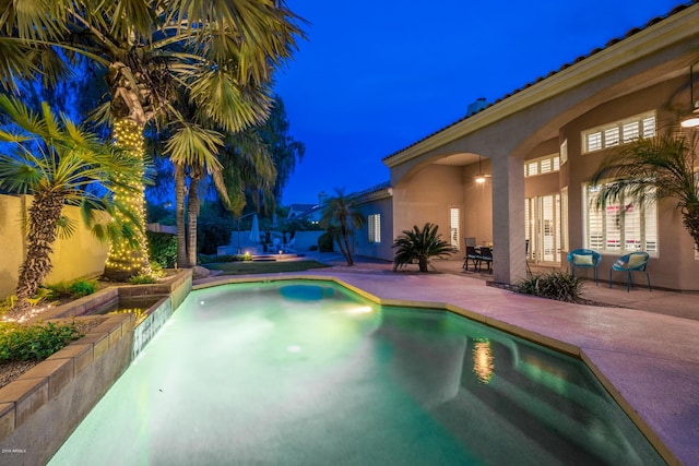 pool at twilight with an in ground hot tub, a patio area, and a fenced backyard