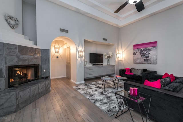 living room featuring arched walkways, visible vents, a tiled fireplace, and hardwood / wood-style flooring