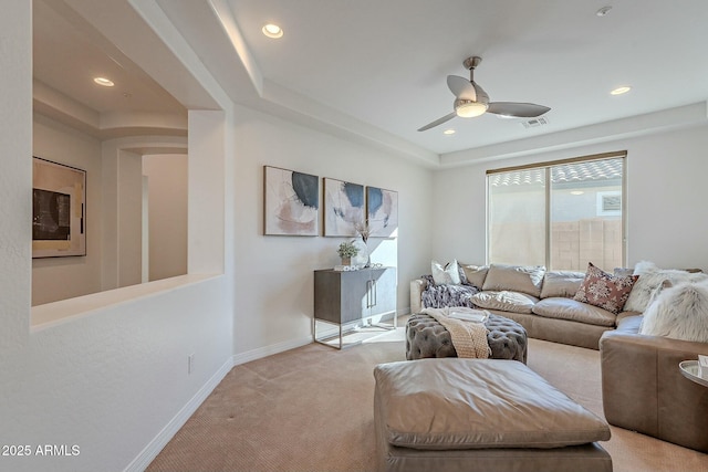 living room with a tray ceiling, ceiling fan, and light carpet