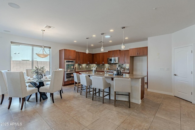 kitchen featuring hanging light fixtures, decorative backsplash, light stone countertops, appliances with stainless steel finishes, and a kitchen bar