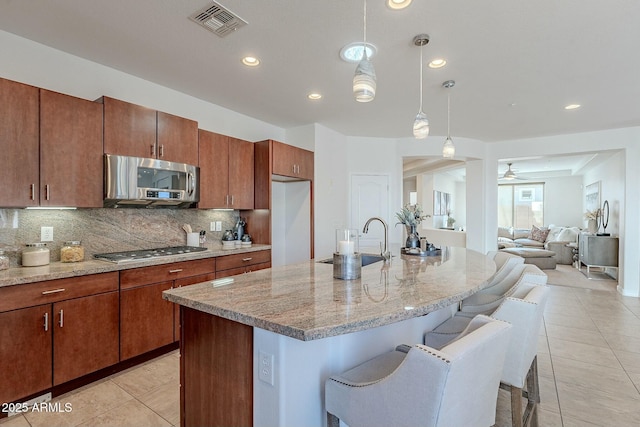 kitchen with a kitchen island with sink, sink, hanging light fixtures, a kitchen bar, and stainless steel appliances