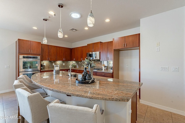 kitchen with backsplash, a center island with sink, light tile patterned floors, appliances with stainless steel finishes, and decorative light fixtures