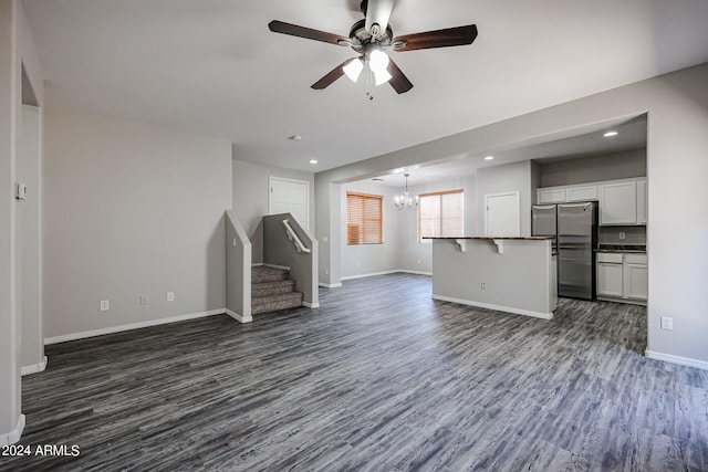 unfurnished living room with ceiling fan with notable chandelier and dark wood-type flooring