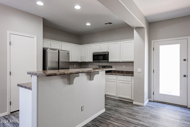 kitchen with white cabinets, a center island, appliances with stainless steel finishes, dark hardwood / wood-style floors, and a breakfast bar