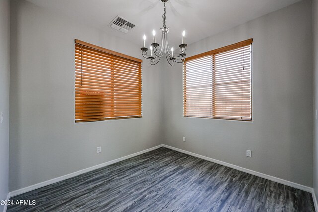 spare room with a notable chandelier and dark wood-type flooring