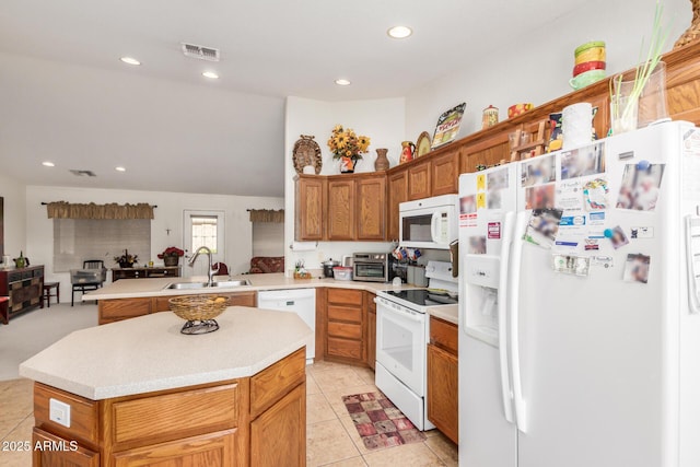 kitchen featuring a peninsula, white appliances, a sink, visible vents, and light countertops