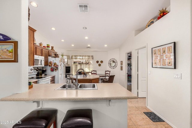 kitchen with light countertops, visible vents, a sink, white appliances, and a peninsula