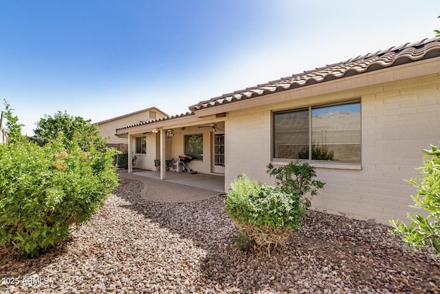 back of property with a tiled roof, brick siding, and a patio area