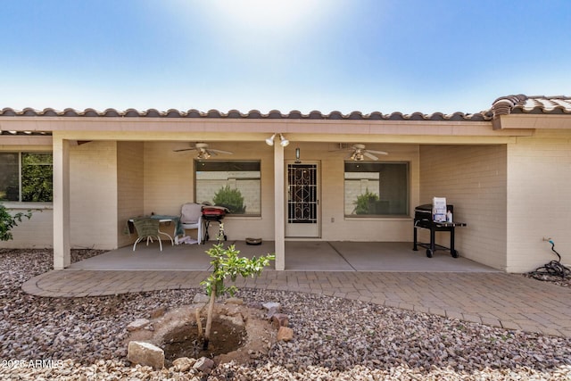 view of exterior entry featuring a patio area, a tiled roof, a ceiling fan, and brick siding