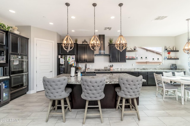 kitchen featuring wall chimney range hood, appliances with stainless steel finishes, light stone counters, and pendant lighting