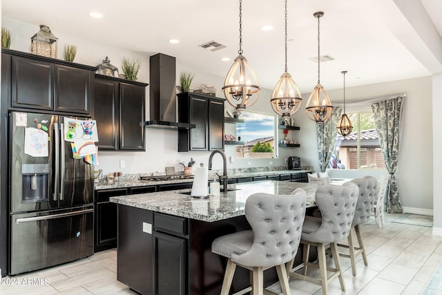 kitchen with light stone countertops, pendant lighting, wall chimney exhaust hood, and stainless steel appliances