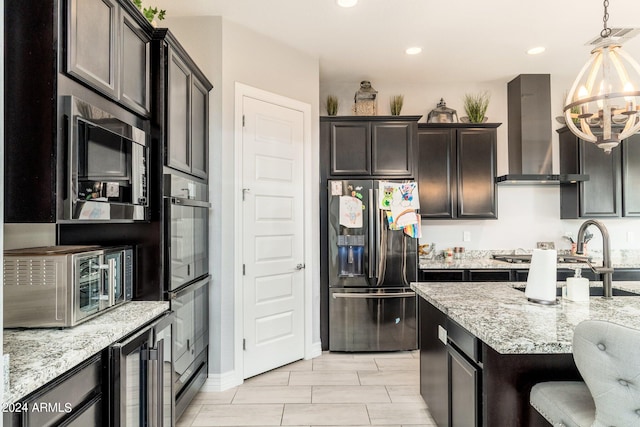 kitchen featuring appliances with stainless steel finishes, a notable chandelier, light stone countertops, wall chimney range hood, and hanging light fixtures