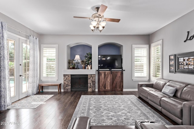living area with ceiling fan, wood-type flooring, french doors, baseboards, and a stone fireplace