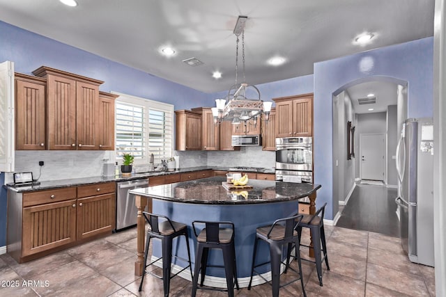 kitchen featuring stainless steel appliances, a kitchen island, arched walkways, a kitchen breakfast bar, and decorative backsplash