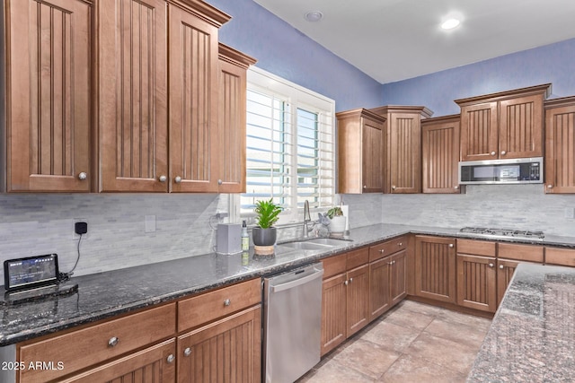 kitchen featuring appliances with stainless steel finishes, a sink, tasteful backsplash, and dark stone counters