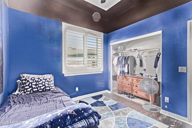bedroom with wood finished floors, baseboards, and a closet