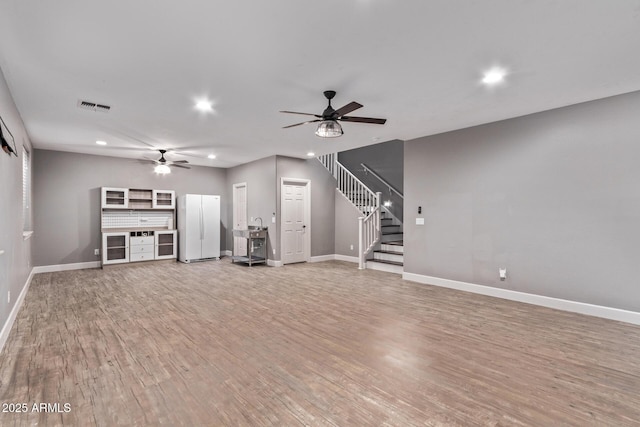 unfurnished living room featuring ceiling fan, recessed lighting, stairway, light wood-type flooring, and baseboards