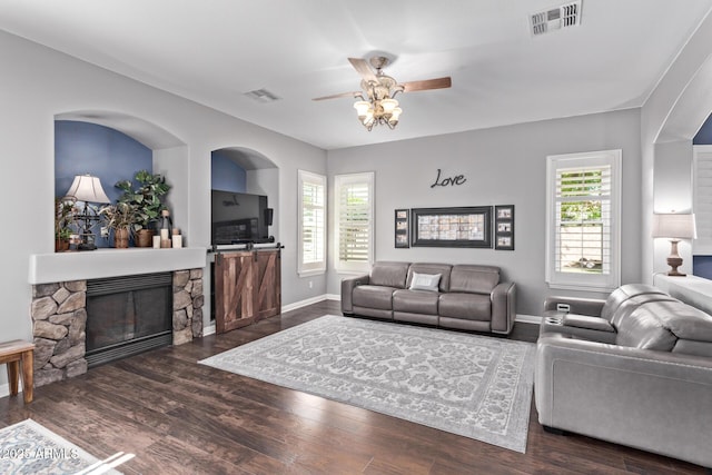 living area featuring healthy amount of natural light, ceiling fan, wood finished floors, and a stone fireplace