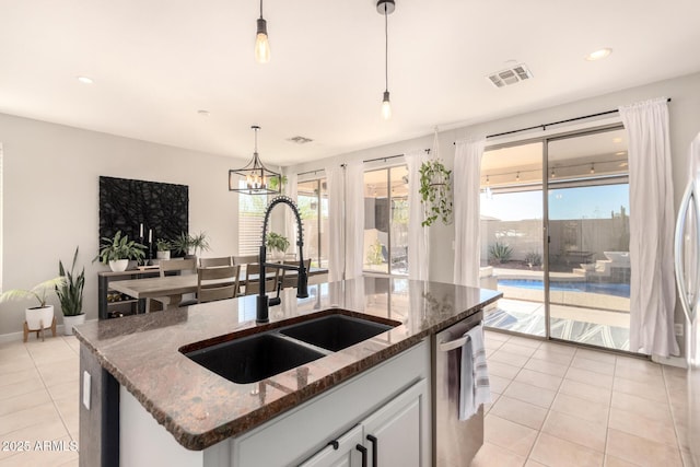 kitchen featuring stainless steel dishwasher, sink, white cabinets, hanging light fixtures, and an island with sink