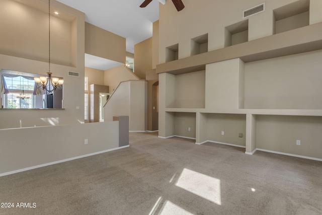 unfurnished living room featuring ceiling fan with notable chandelier, a high ceiling, and light colored carpet