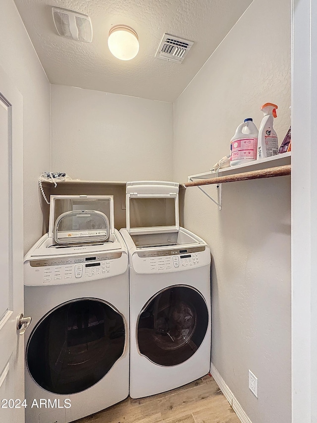 clothes washing area with separate washer and dryer, a textured ceiling, and light hardwood / wood-style flooring