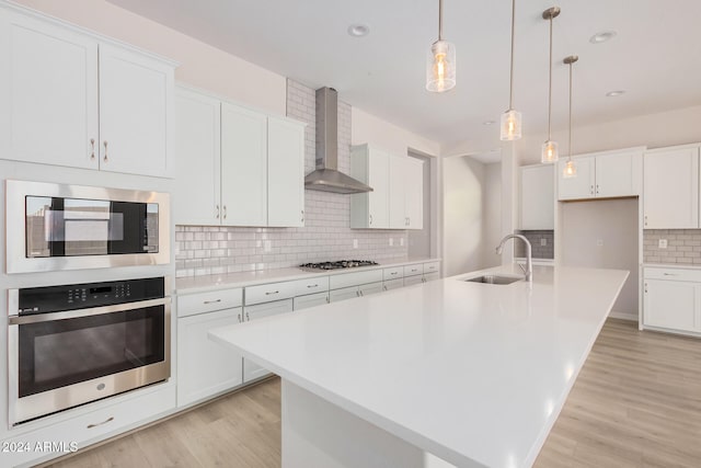 kitchen with stainless steel appliances, white cabinetry, sink, a kitchen island with sink, and wall chimney range hood