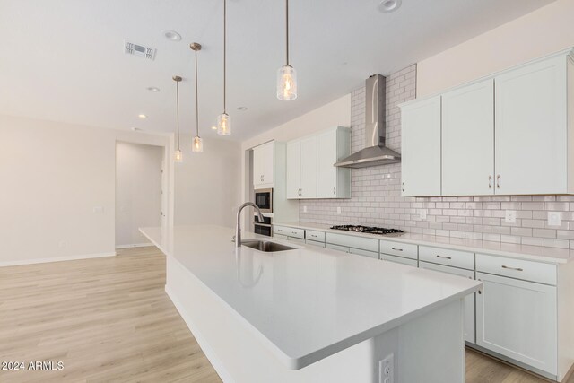 kitchen featuring wall chimney range hood, white cabinets, stainless steel gas stovetop, and a kitchen island with sink