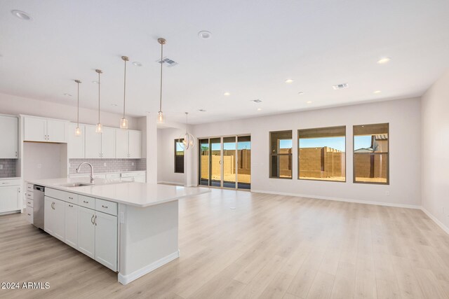 kitchen with light hardwood / wood-style floors, a center island with sink, sink, white cabinetry, and decorative light fixtures