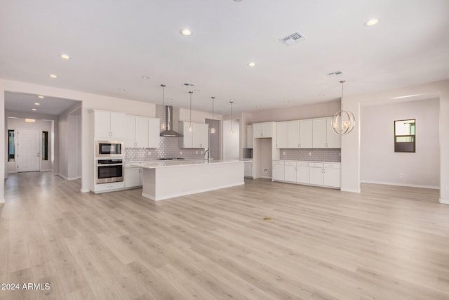 kitchen with light hardwood / wood-style floors, a center island with sink, oven, wall chimney range hood, and white cabinetry