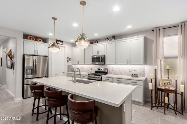 kitchen featuring decorative light fixtures, a center island with sink, sink, white cabinetry, and appliances with stainless steel finishes